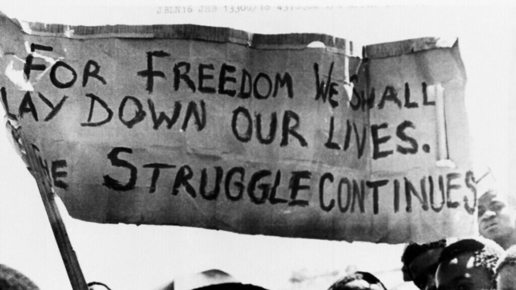 Former South African police officers convicted for 1987 killing of anti-apartheid activist FILE - A banner is held aloft above black students in Johannesburg, South Africa, in the township of Soweto where they rallied after the funeral of a 16-year-old black student who died in jail, Oct. 18, 1976.