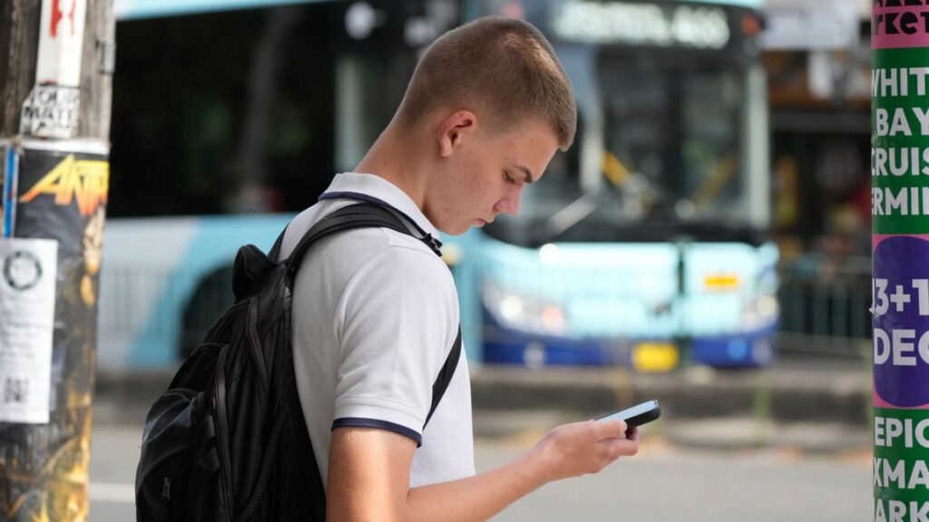 School boy Kyryl Pantovic uses his phone as he waits to cross the street in Sydney, Monday, Dec. 8, 2025